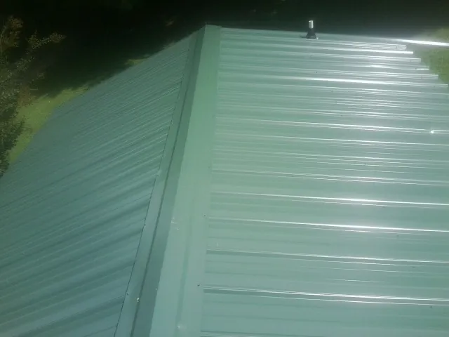 New green metal panels meeting at the ridge of a roof — Flat Roof Repair work by our crew in Rantoul
