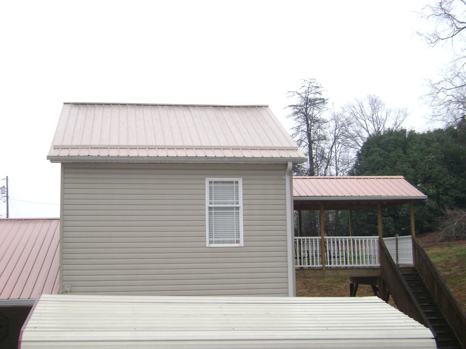 Tan metal roofs on a two story addition and attached porch, from a Roof Replacement job in Rantoul